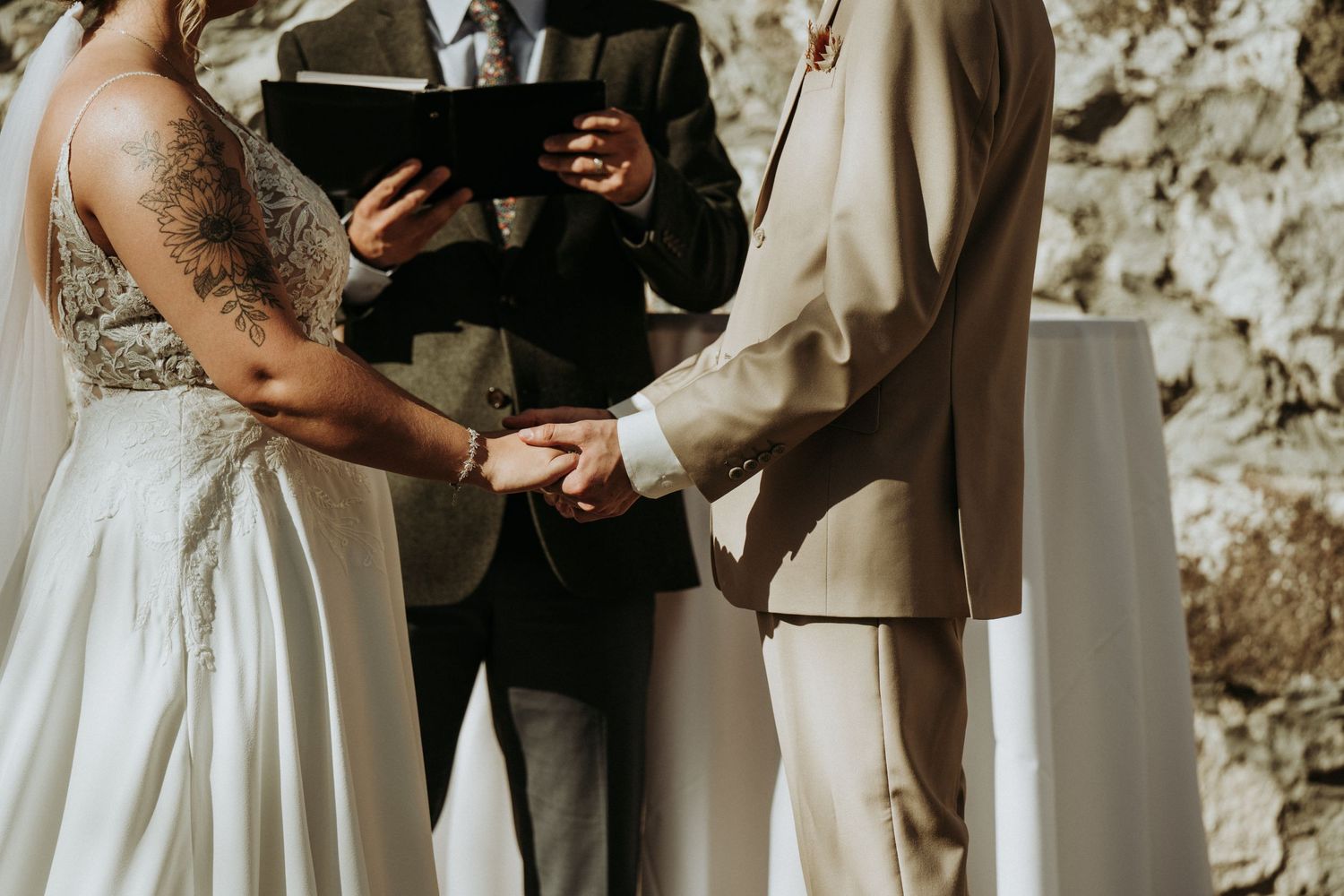 Close up of bride and groom holding hands during outdoor wedding ceremony during their exchange of rings.