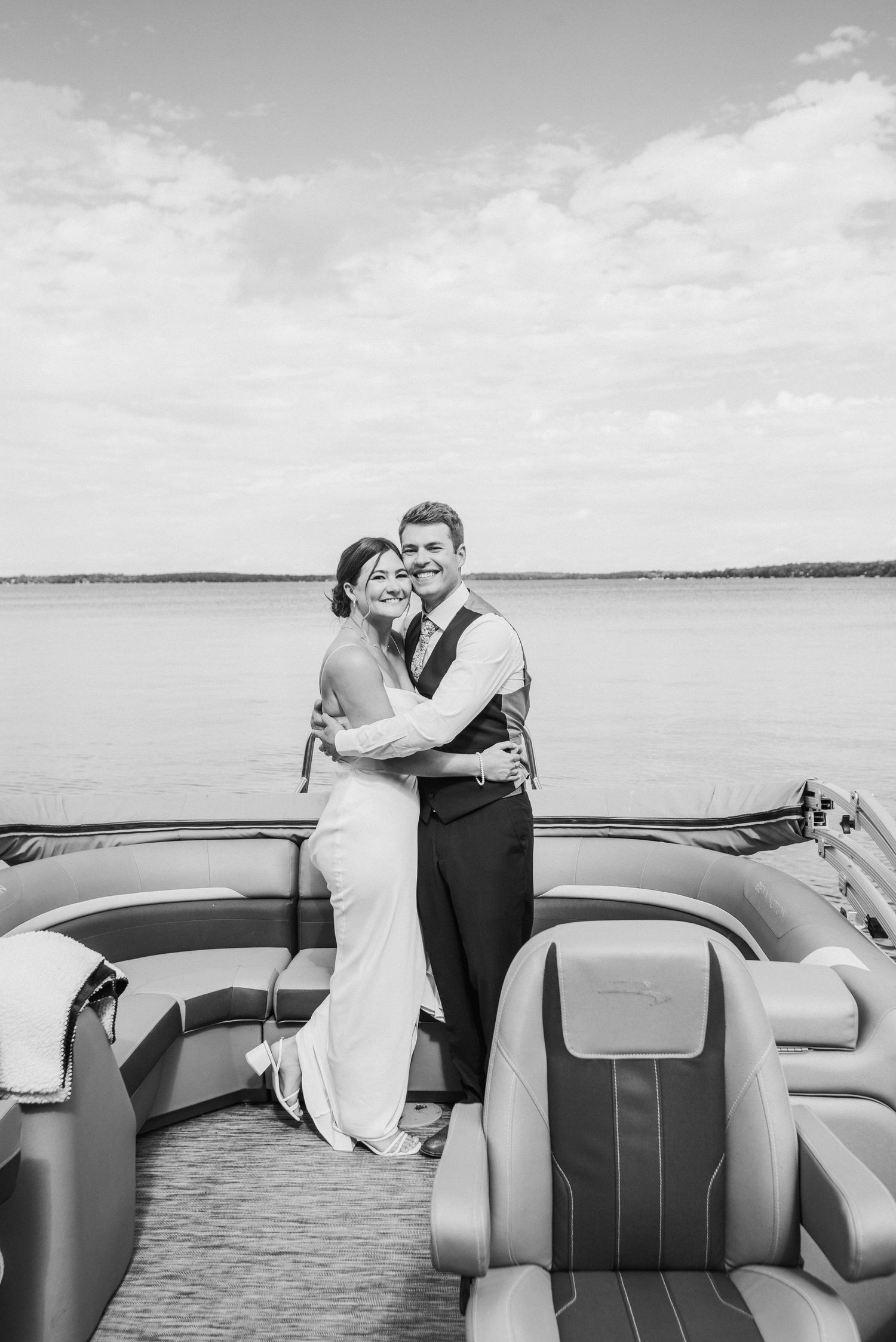 A black and white photo of a romantic couple embracing on a boat deck with lake and sky in the background. 
Battle Lake MN