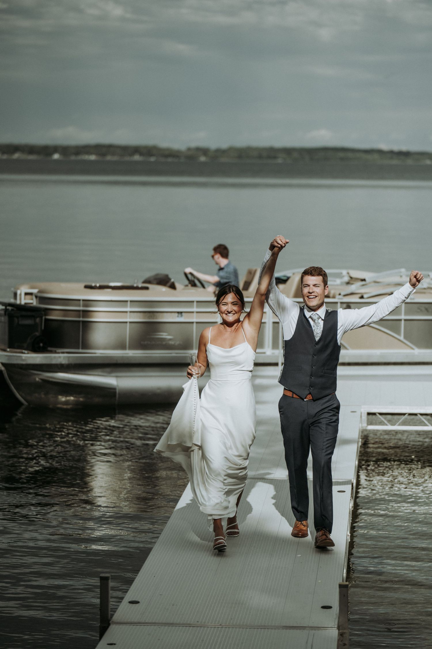 Wedding couple celebrating on a boat dock with pontoon boats in the background on an overcast day at the lake. 
Battle Lake MN 
Lake wedding