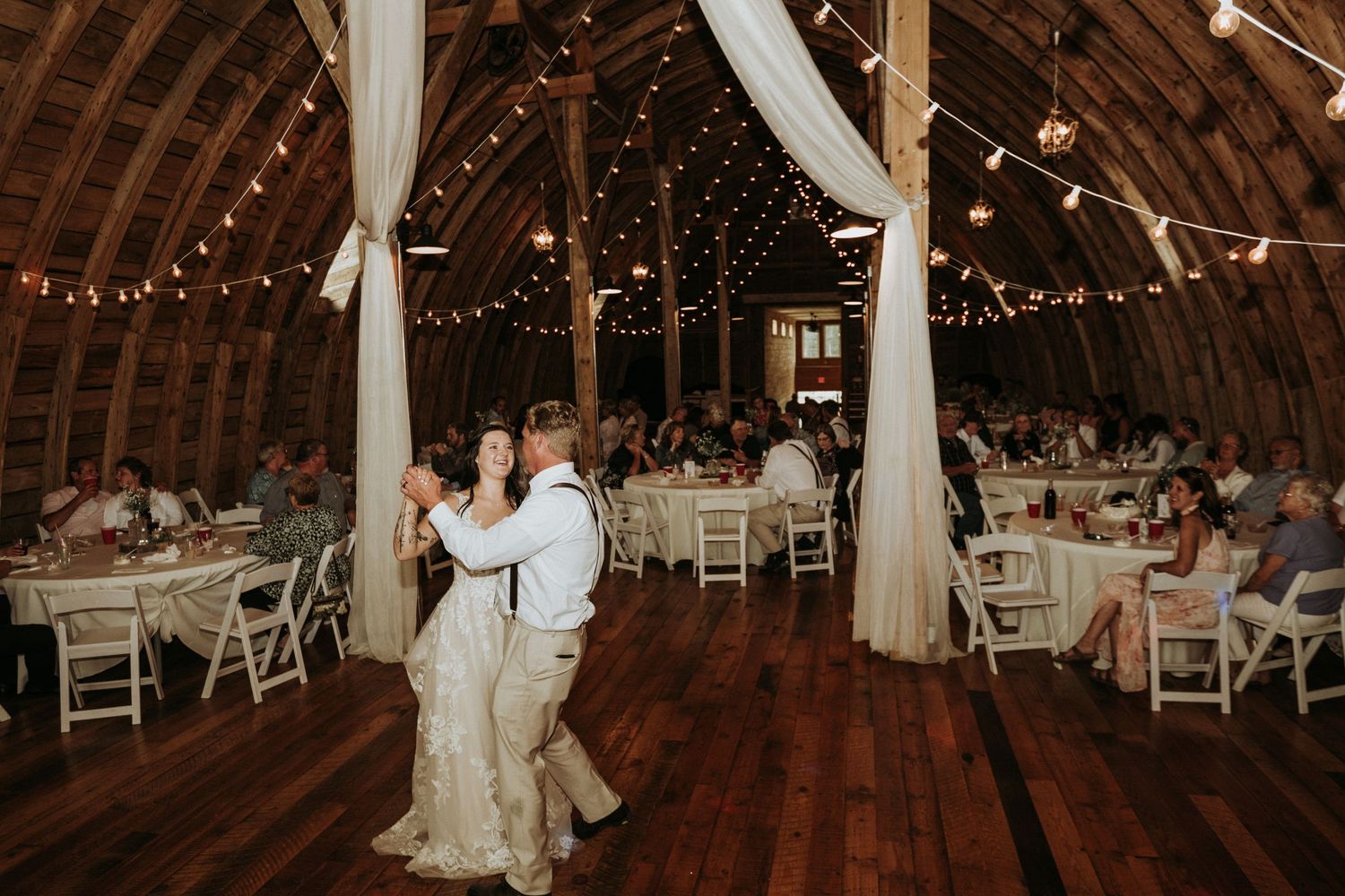 Dancing and celebration inside a rustic barn decorated with string lights during a wedding reception. 
Stone Hill Farm in Eagle Bend MN.