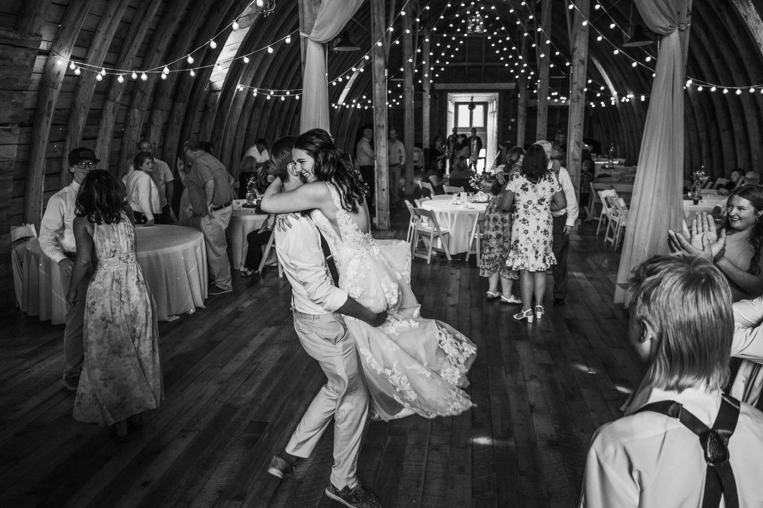 Dancing and celebration inside a rustic barn decorated with string lights during a wedding reception. 
Stone Hill Farm in Eagle Bend MN.