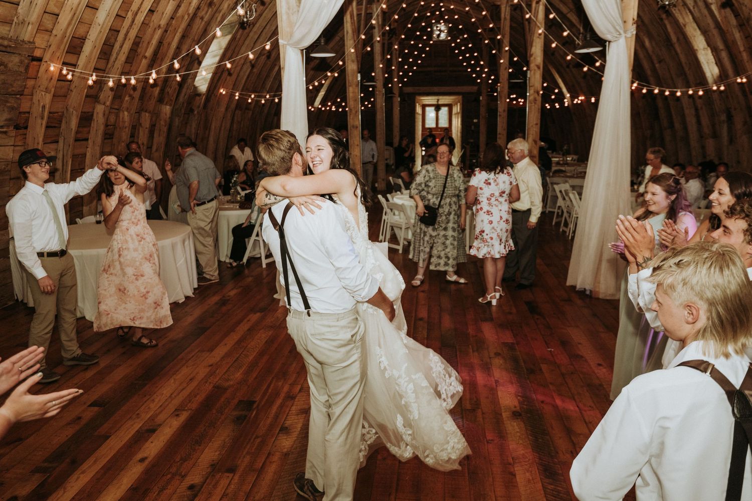 Dancing and celebration inside a rustic barn decorated with string lights during a wedding reception. 
Stone Hill Farm in Eagle Bend MN.