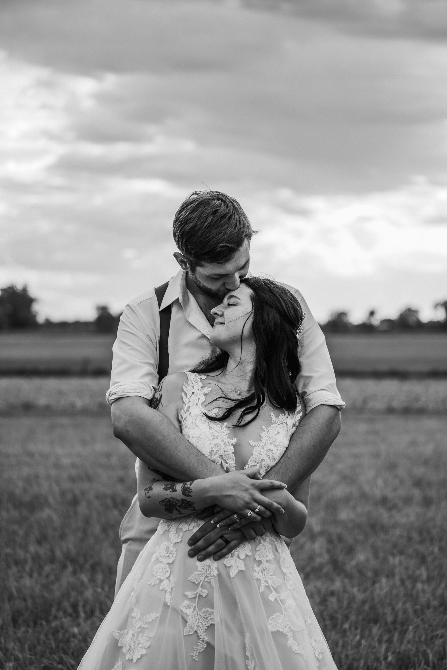 a black and white photo of a husband wrapping his arms around his wife and as they hold each other during golden hour.