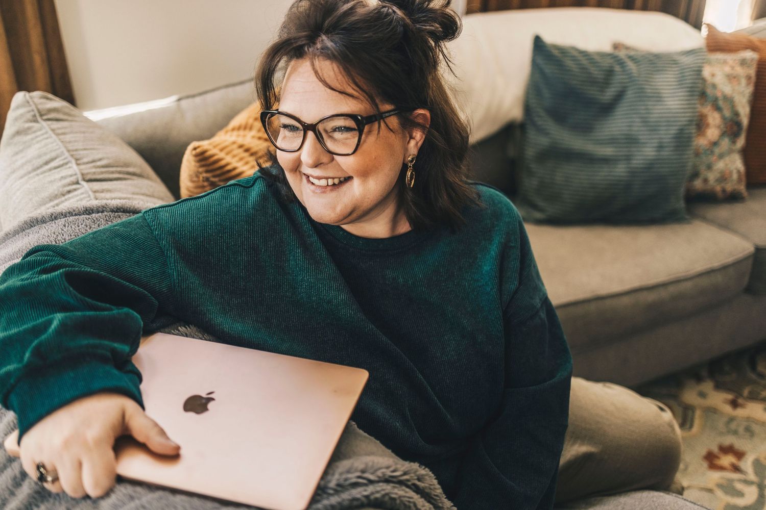 Smiling woman in green sweater holding Apple iPad while relaxing on couch.
