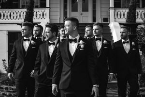 Black and white photo of groomsmen in tuxedos posing together outside a mansion.
