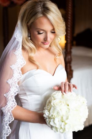 Bride in white lace veil holds a round bouquet of white flowers.