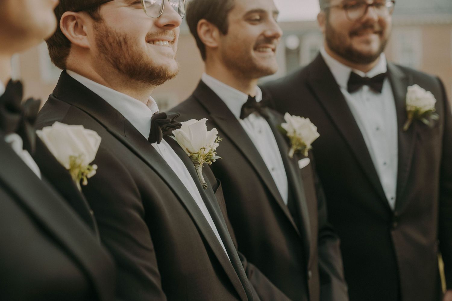 Three groomsmen in black tuxedos with white boutonnieres pose together in a candid wedding moment.