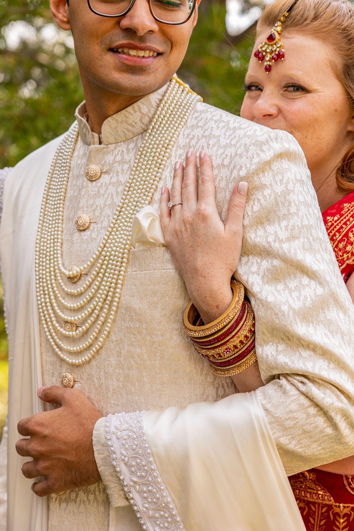 Traditional Indian wedding attire featuring ornate white sherwani with pearl necklaces and red accents.