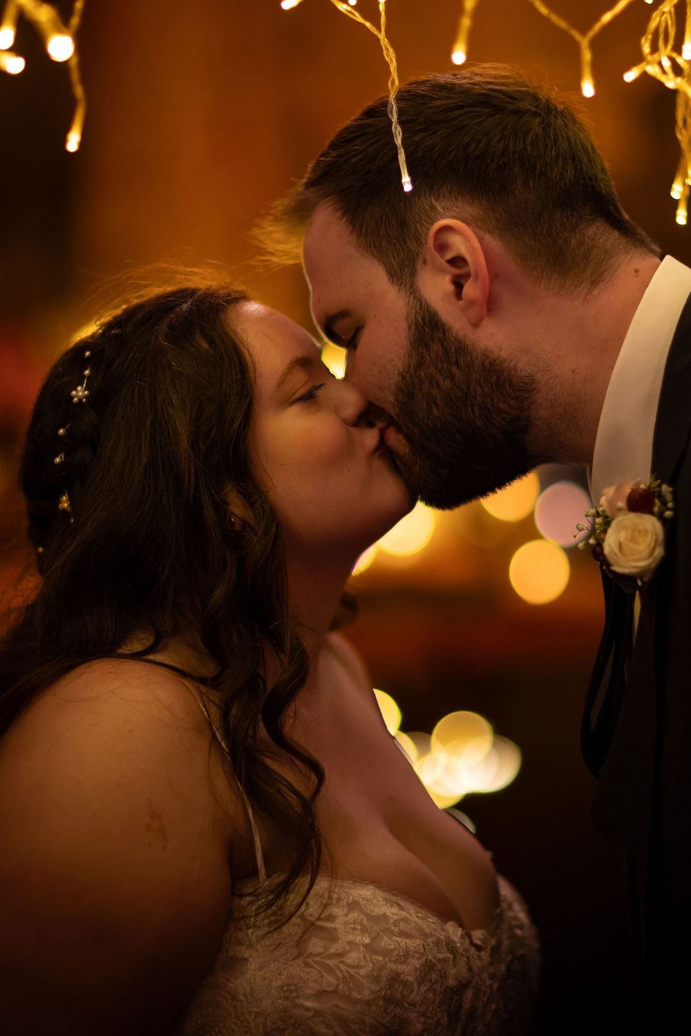 Romantic silhouette of newlyweds kissing under warm glowing lights at their wedding reception.