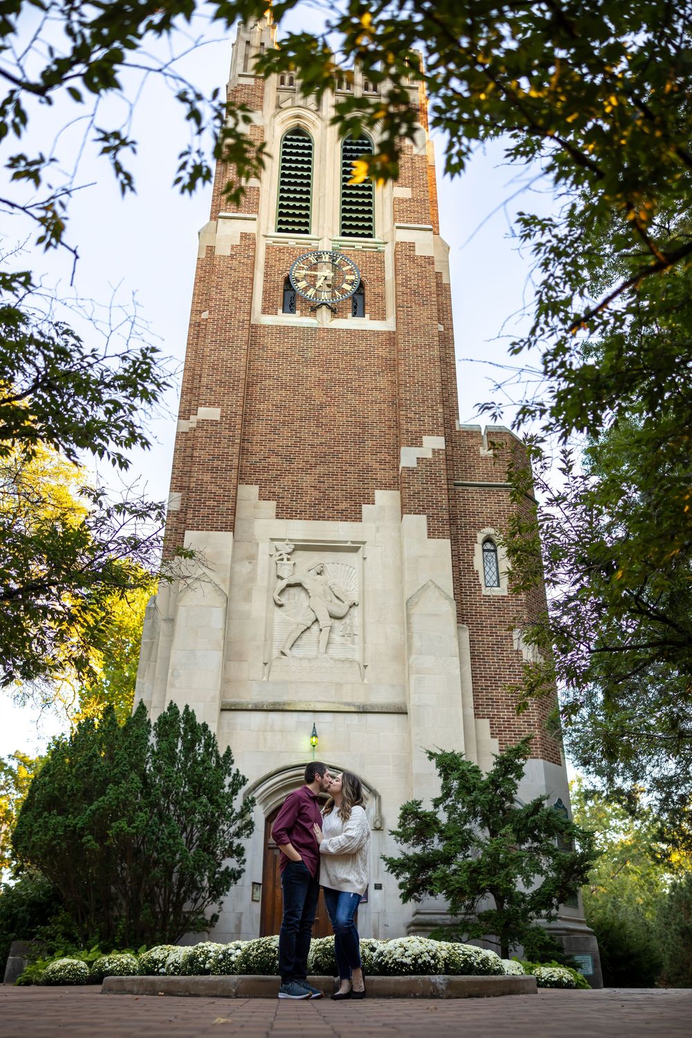 Couple posing for romantic photos against brick church architecture at sunset.