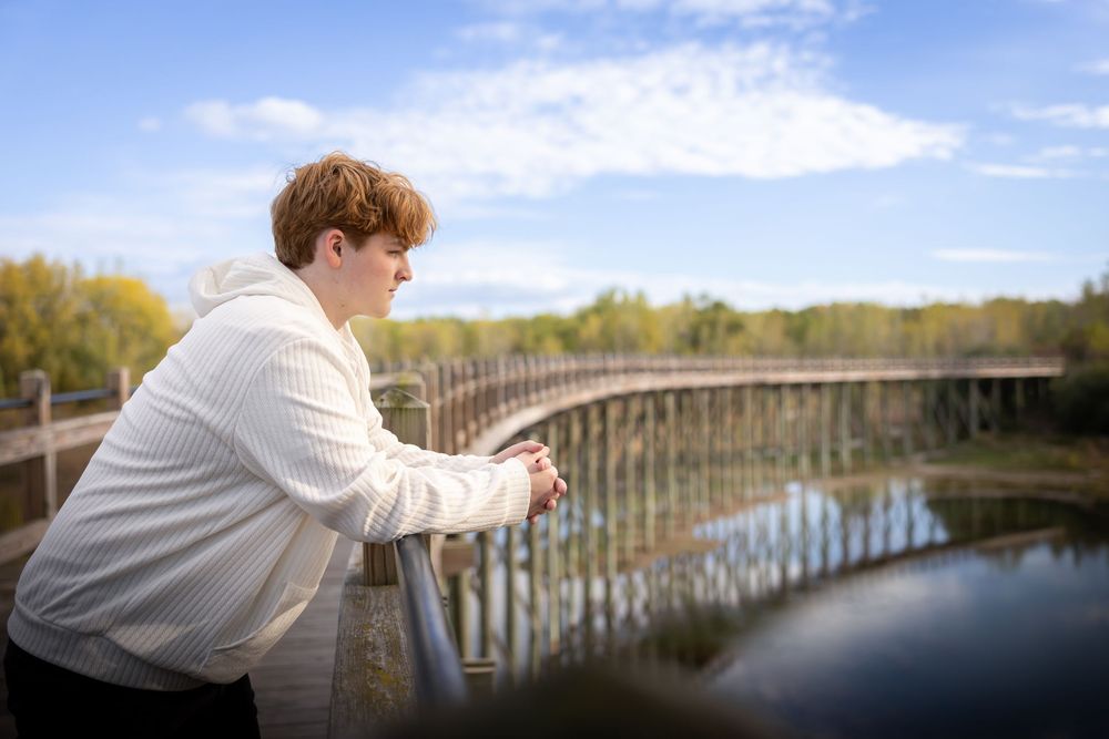 Person in white sweater looking contemplatively over bridge railing in autumn park.