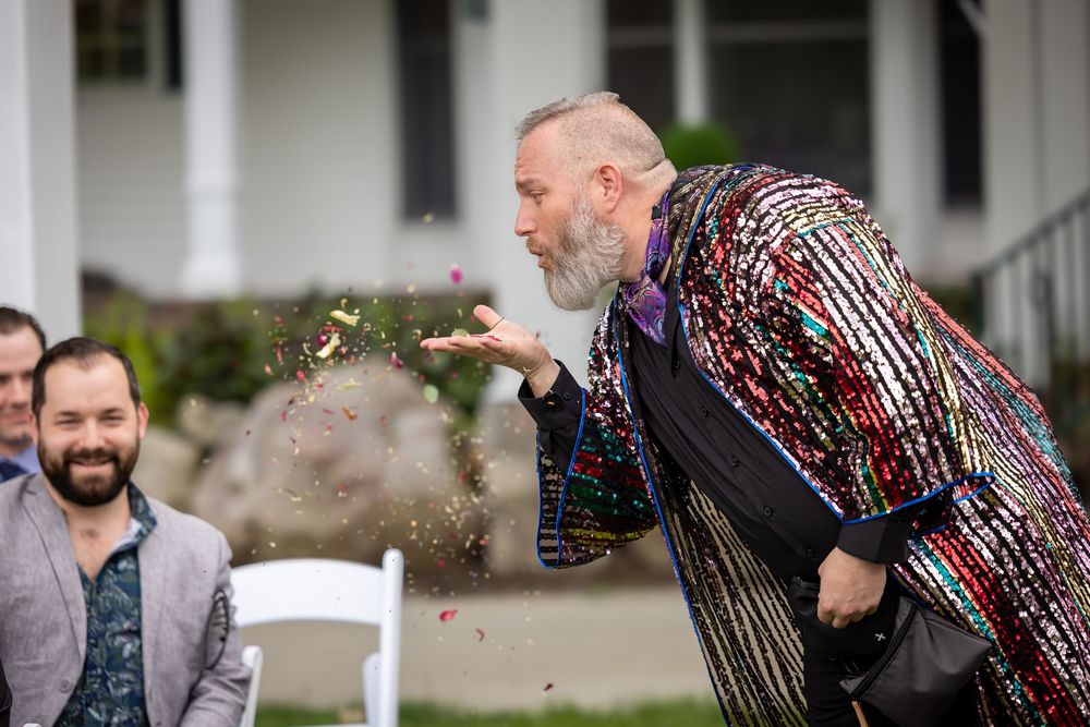 A performer in a sparkly jacket blows glitter into the air while entertaining guests at an outdoor event.
