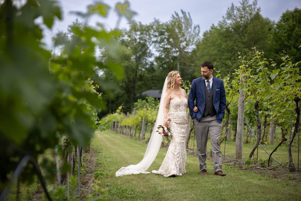 A couple in wedding attire poses together in a lush green vineyard setting during their special day.