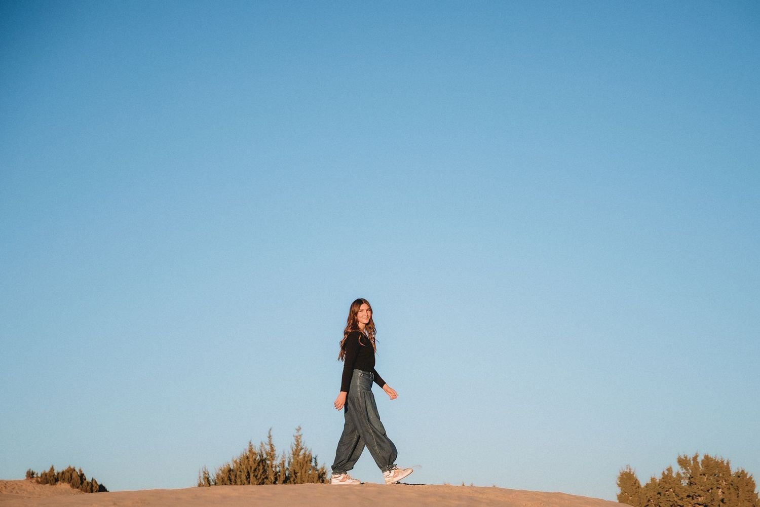American fork high school senior girls silhouettes against blue sky during outdoor portrait session.