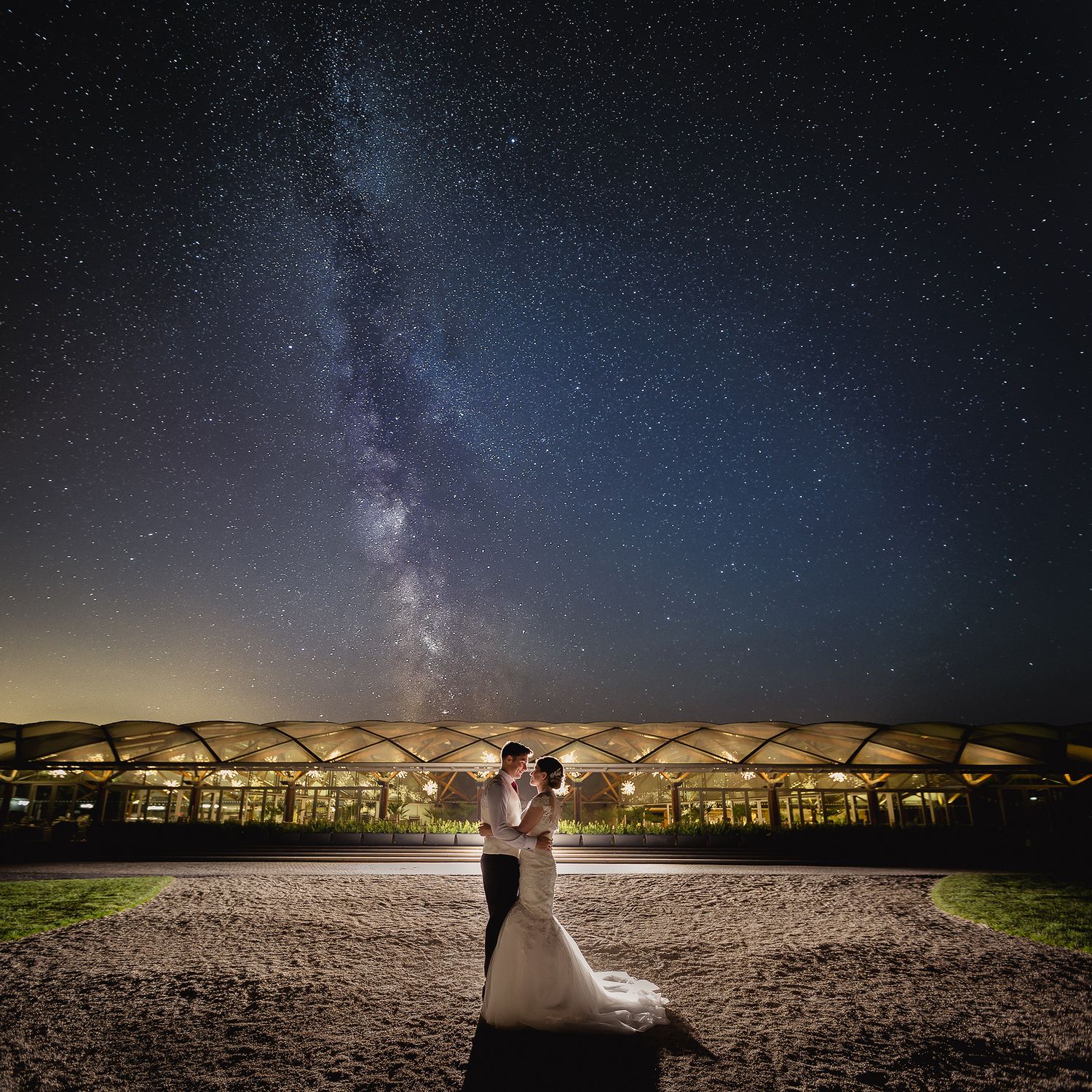 Starlit night sky wedding photo with couple silhouetted against illuminated beach umbrellas.