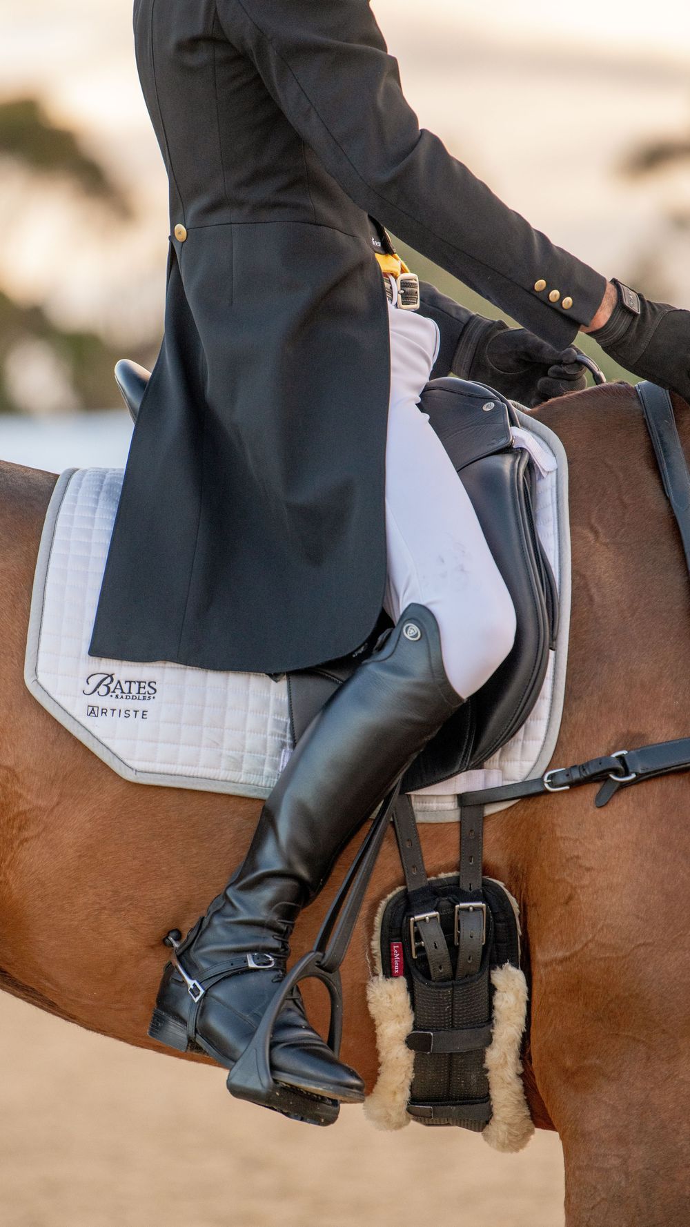 Equestrian rider in black coat and tall leather boots seated on a chestnut horse with a Bates Artiste saddle pad.