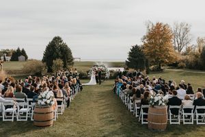 A panoramic view of an outdoor wedding ceremony setup with white chairs and rustic wooden decor in an autumn field.