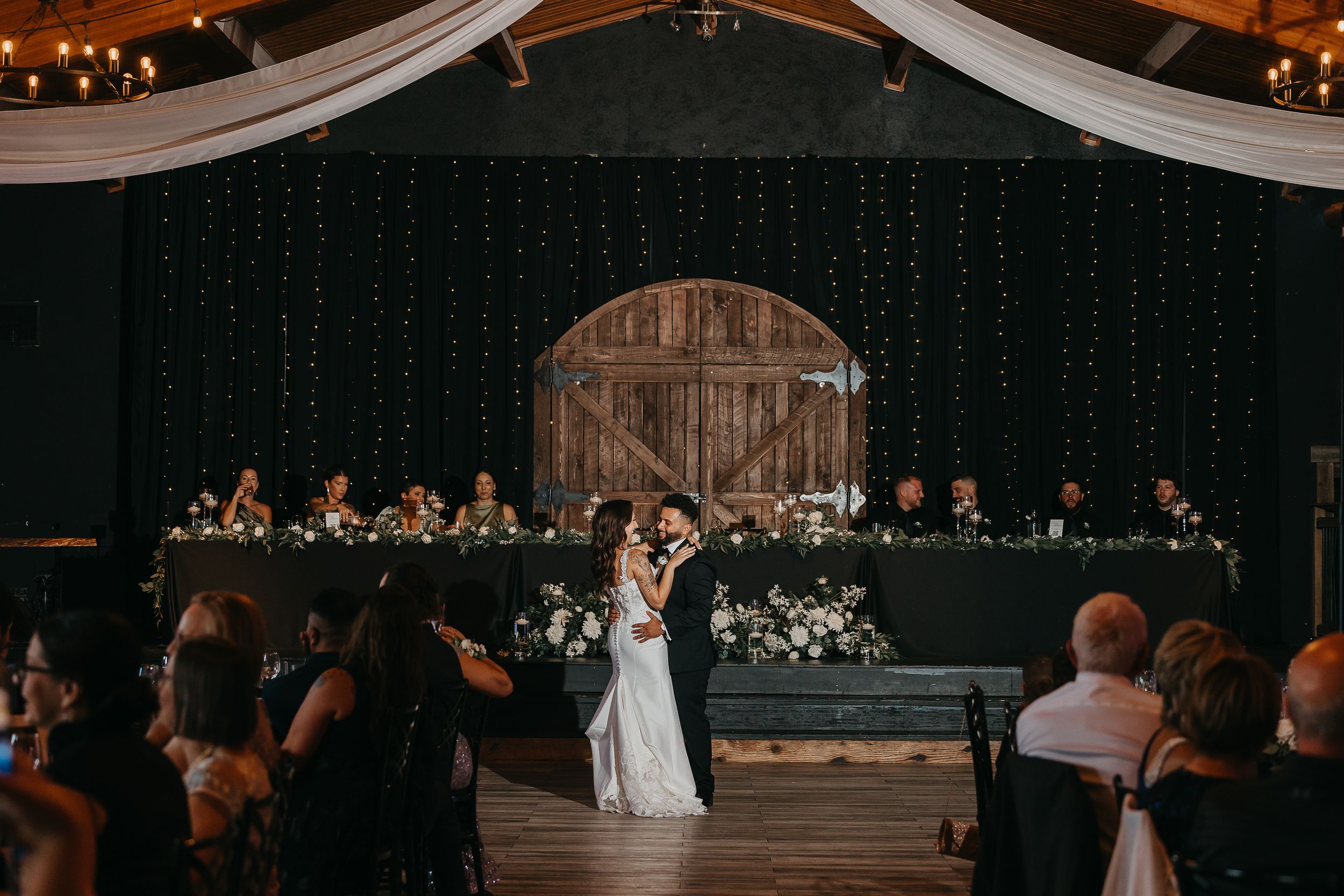 Wedding reception venue decorated with elegant white drapes and warm lighting creates a romantic atmosphere.