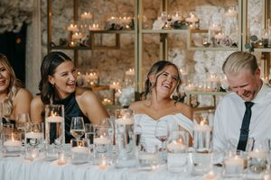 Wedding reception guests share a candid moment of laughter at an elegant candlelit table setting.