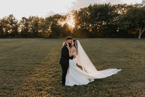 A couple shares romantic moments in a golden sunlit field during sunset as a wedding dress flows in the breeze.