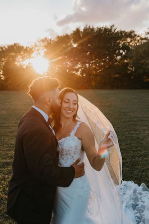 A romantic sunset wedding portrait of a couple embracing outdoors with golden light streaming through trees.