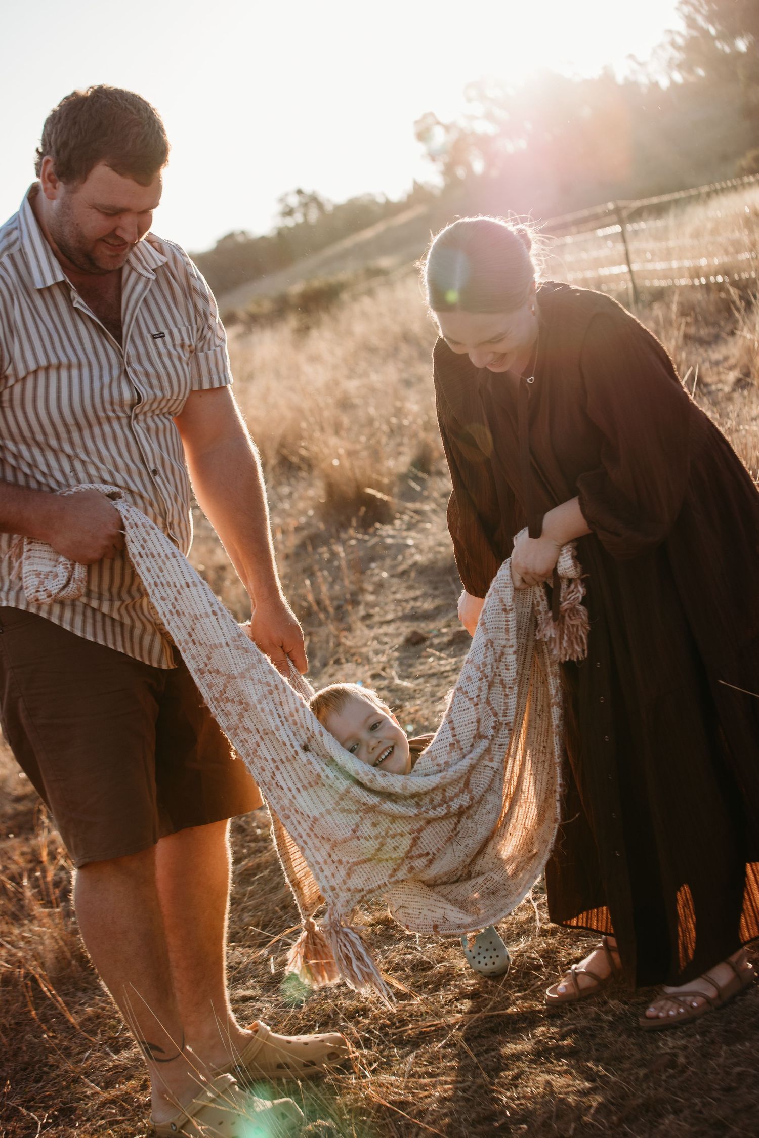 People interacting with blanket or textile in sunlit field during golden hour.