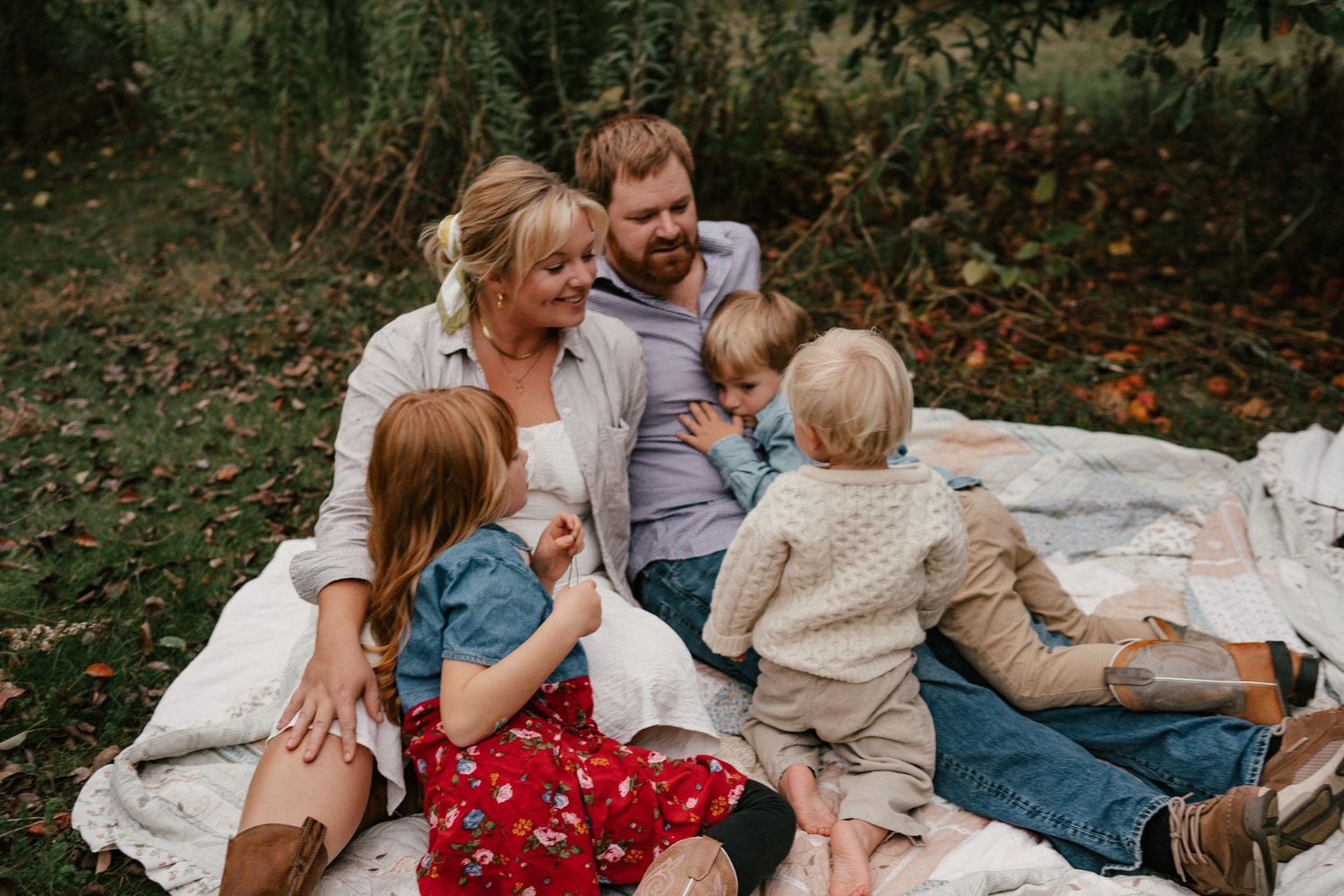 Family having picnic on brown blanket in grassy field with their dog.