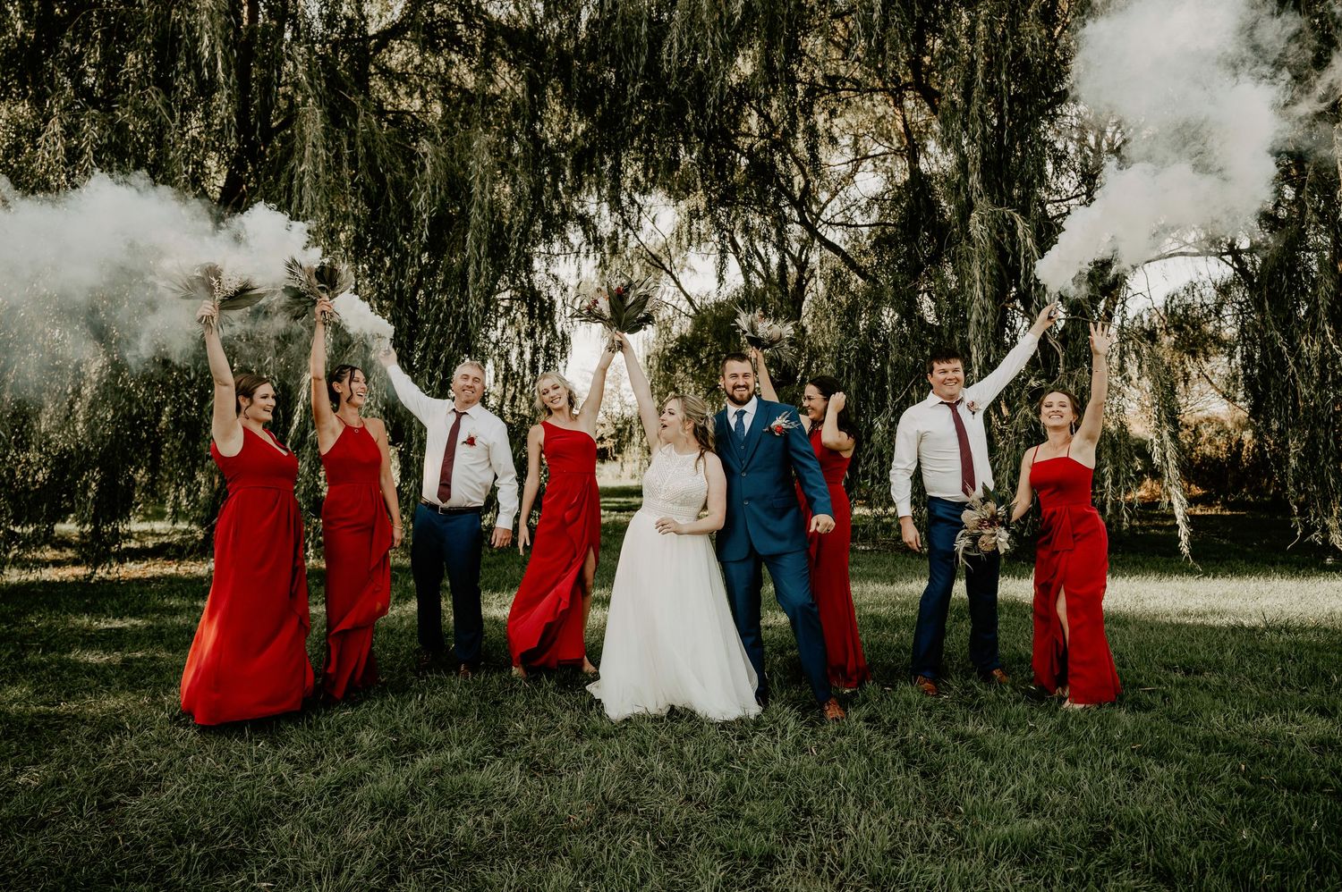 wedding party in red with bride and groom holding smoke