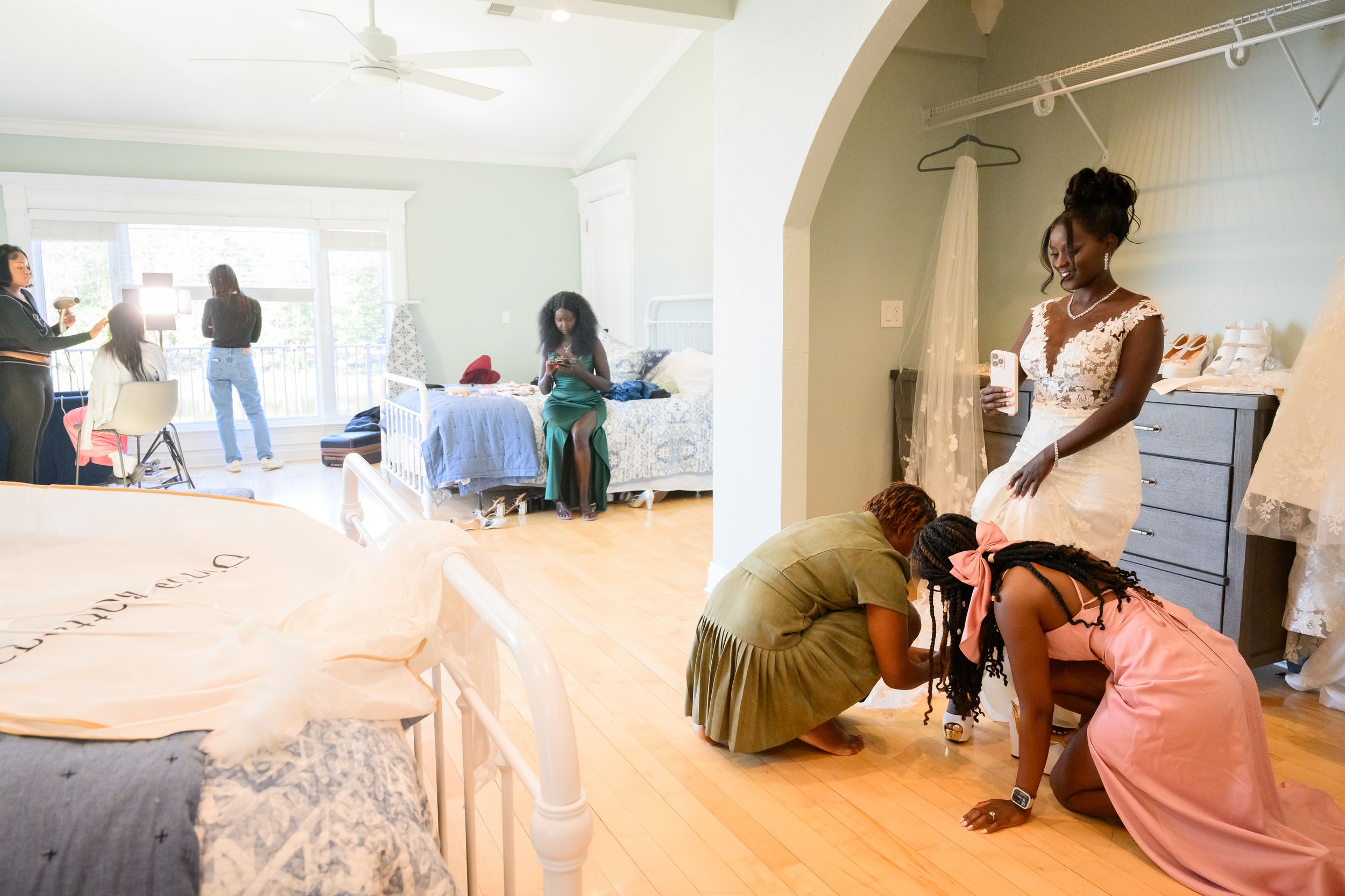 Bride getting dressed with bridesmaids helping in a bright room before wedding ceremony.