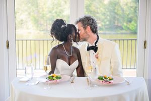 Interracial newlywed couple sharing a kiss at their wedding reception table with champagne glasses and salads.