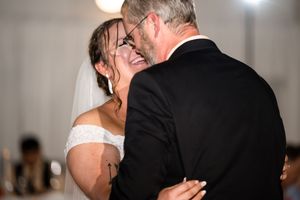 Bride in white veil shares an emotional dance with a man in a black suit at a wedding reception.