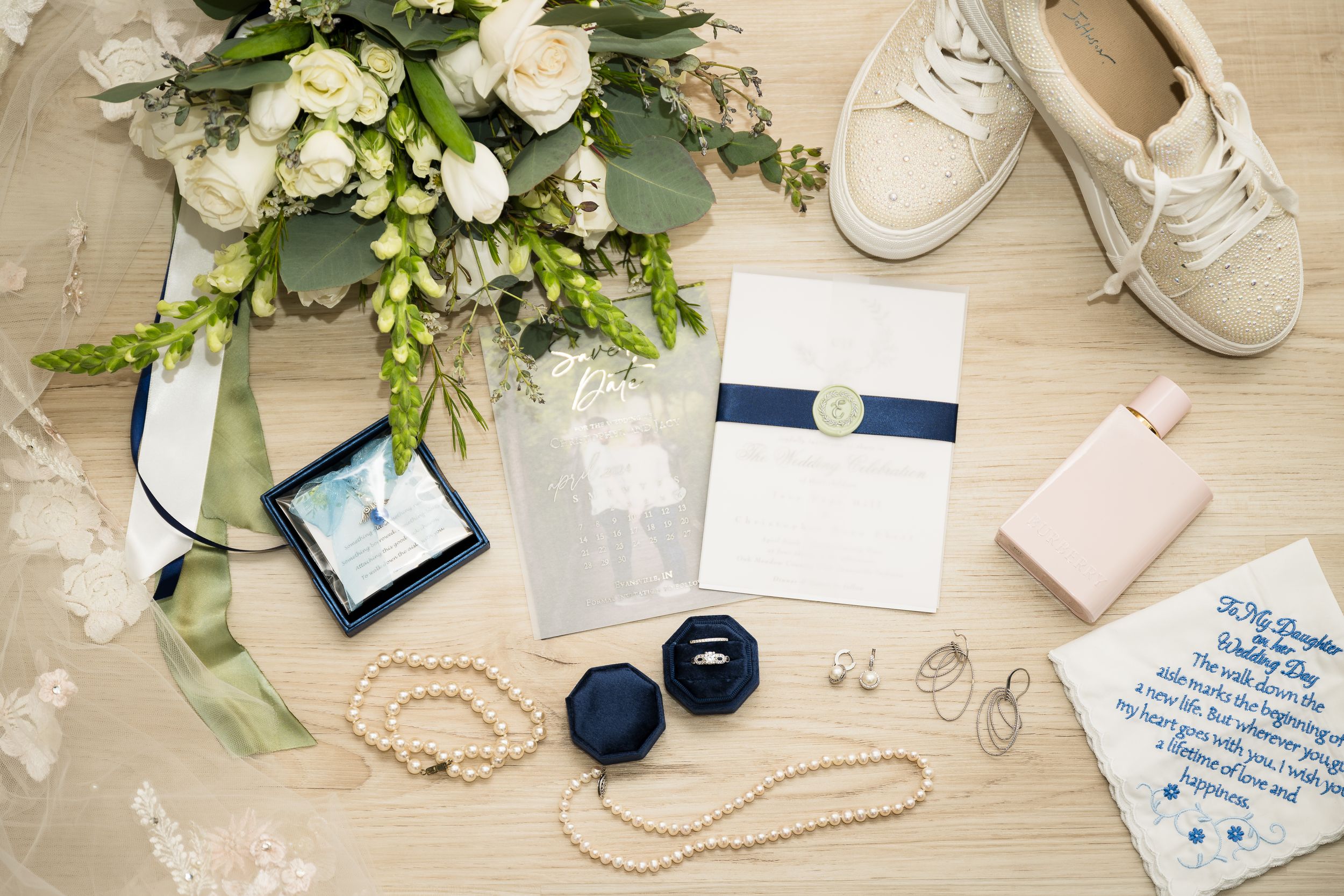 Wedding details flatlay with white florals, navy ring boxes, jewelry and bridal accessories.