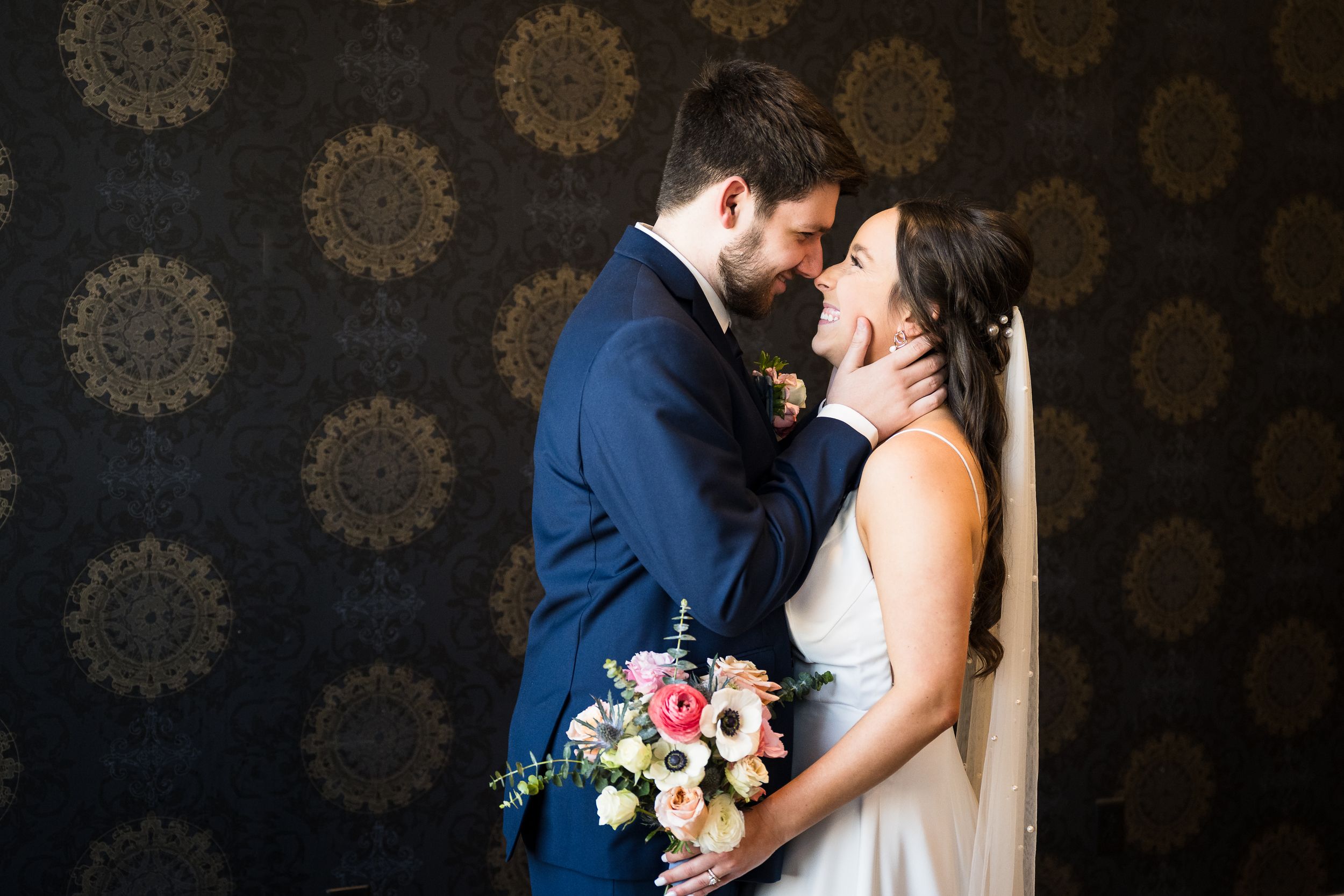 A romantic wedding moment against a dark patterned backdrop with a beautiful floral bouquet.