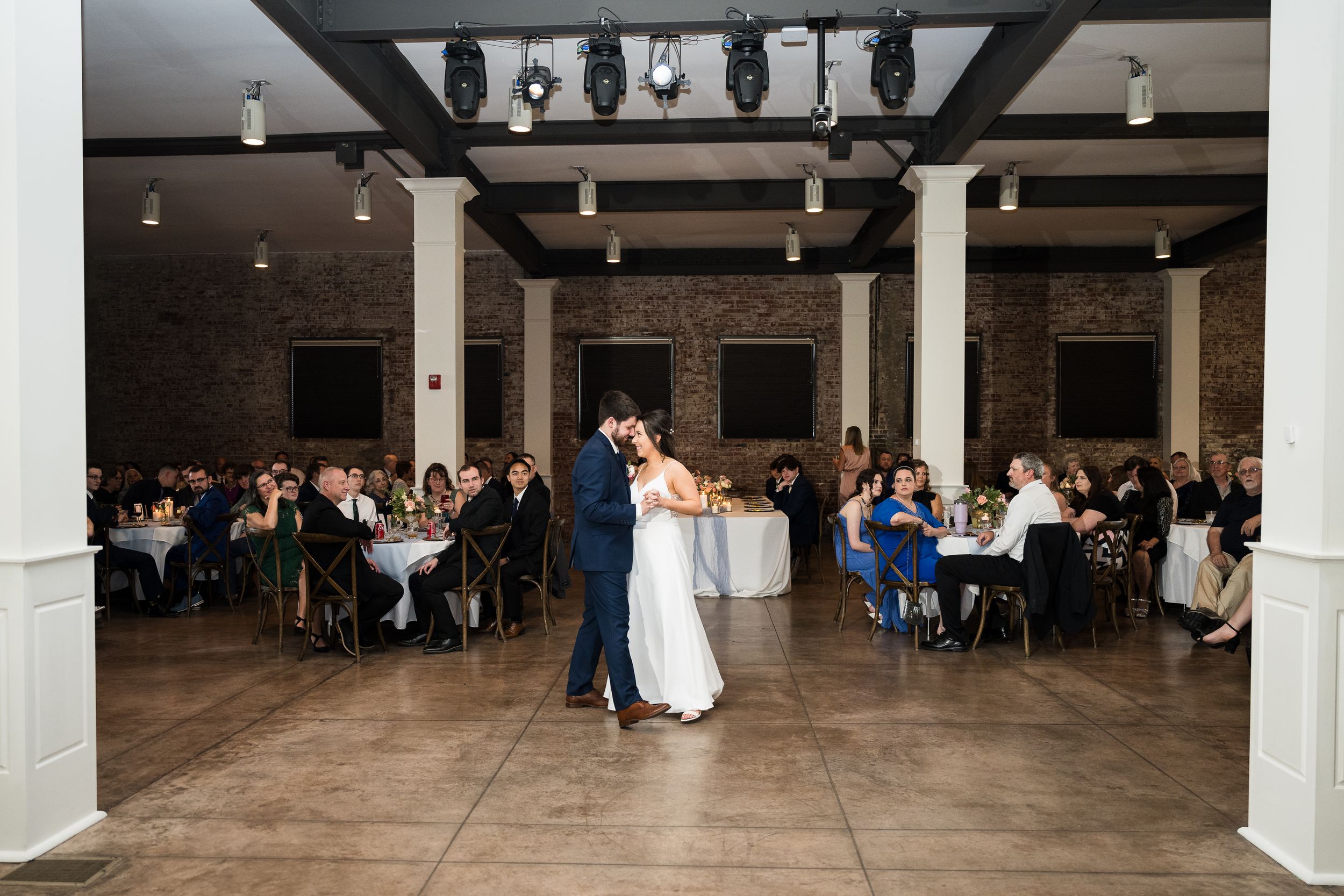 A couple shares their first dance in a spacious reception venue surrounded by guests.