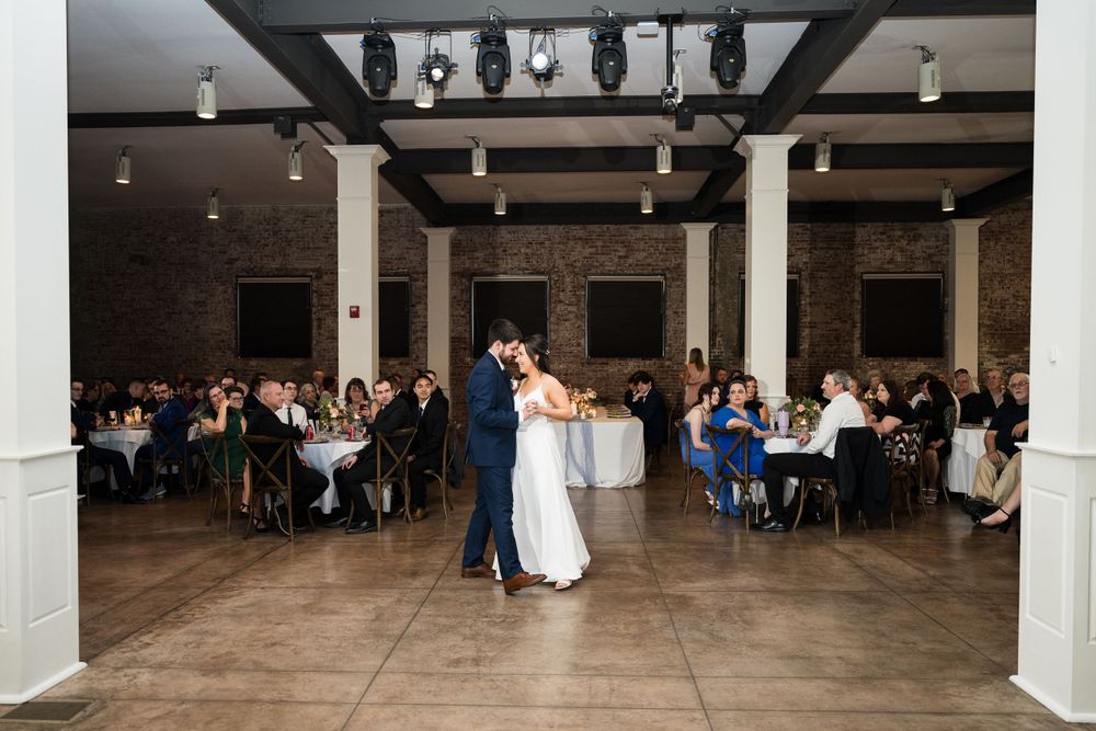 A couple shares their first dance in a spacious reception venue surrounded by guests.