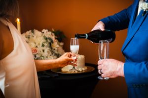 A groom in a blue suit pours champagne into glasses during a wedding reception celebration.