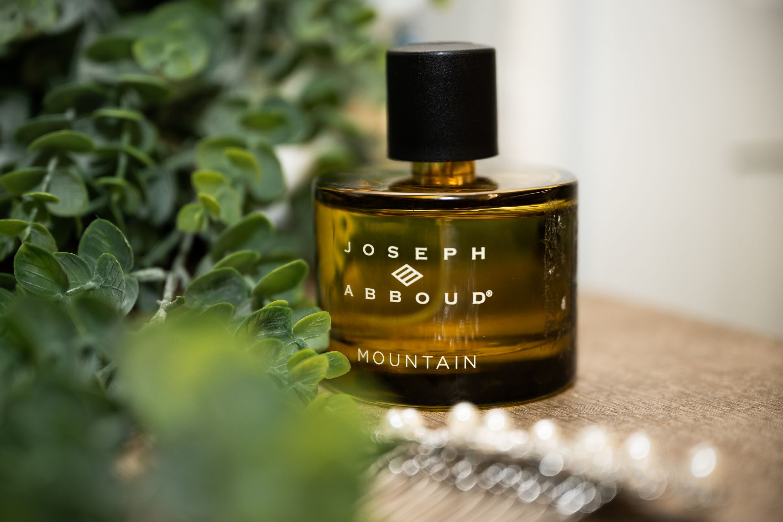 A luxurious Joseph Abboud perfume bottle sits elegantly among green foliage in soft lighting.