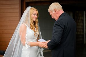 Bride in white gown and veil exchanges vows with groom in black suit during outdoor wedding ceremony.