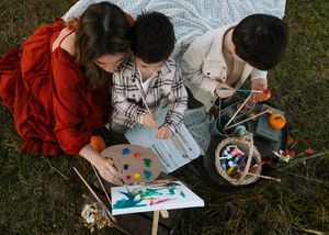 Overhead view of people painting with watercolors while sitting in the grass on a sunny day.