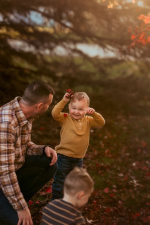 Family playing together outdoors during golden hour among fallen autumn leaves.