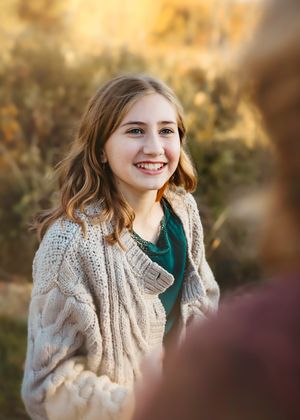 Young woman wearing a cozy knit scarf and green top poses outdoors in warm autumn lighting.