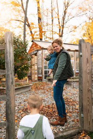 Children watch adults playfully interacting on wooden fence posts surrounded by autumn foliage.