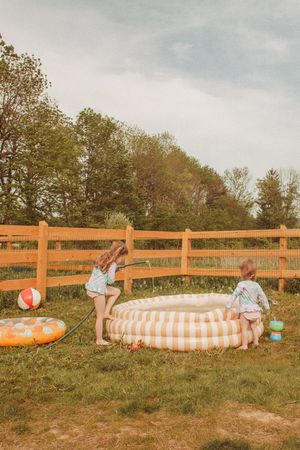 Children playing with a large orange and white striped inflatable pool on a grassy hill during summer.