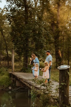 A family walks along a rustic wooden bridge over water in a serene wooded setting during golden hour.