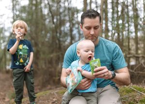 Parent and child sit together in a wooded area while sharing a snack and bonding outdoors.
