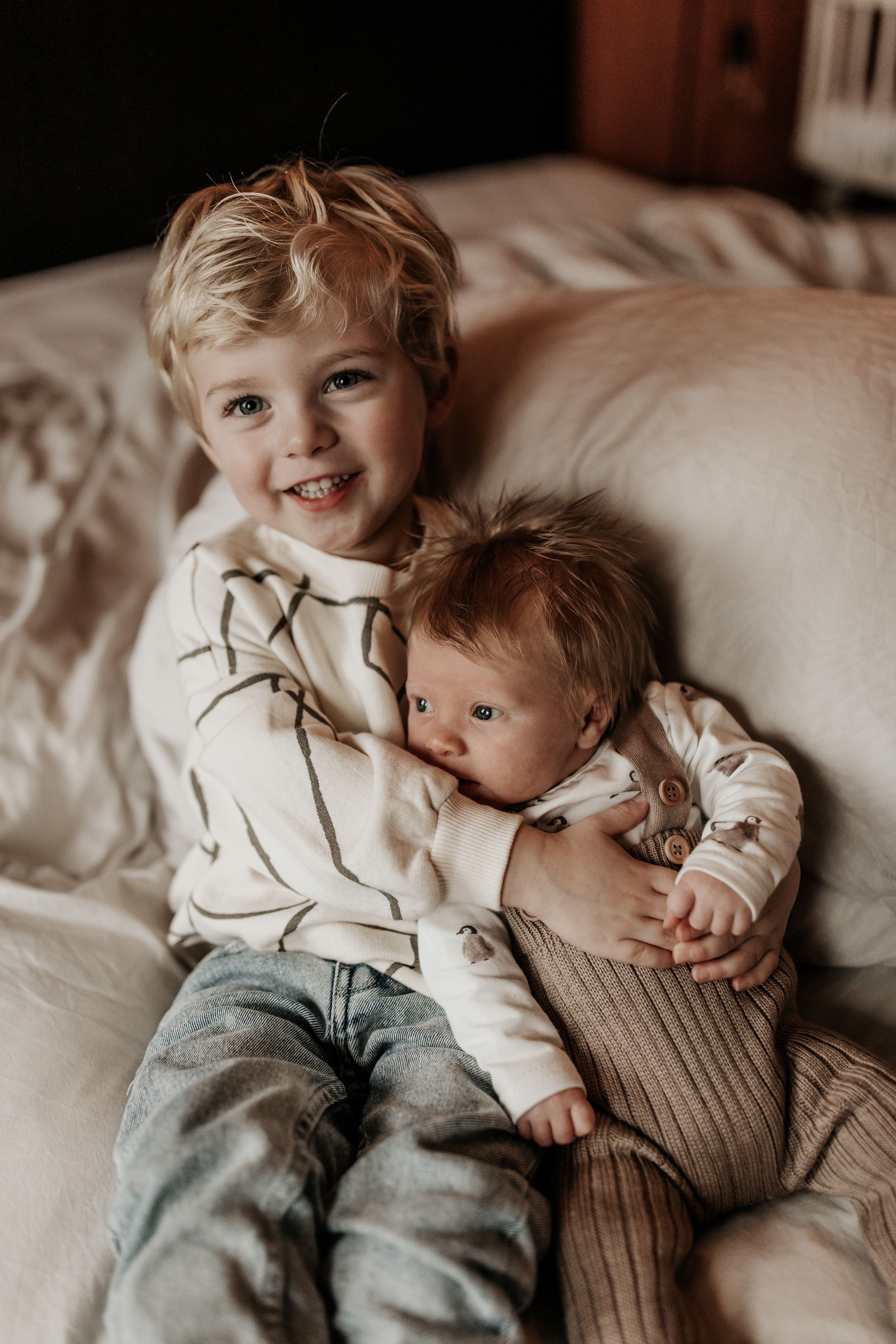Broertje knuffelt met newborn baby in bed