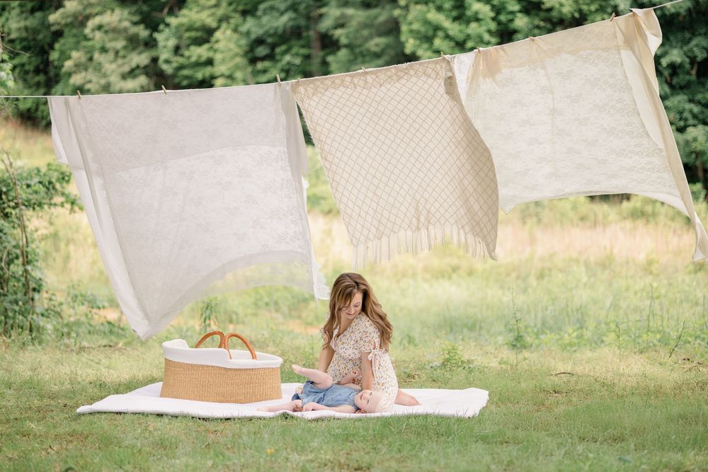 A person sits on a white blanket in a grassy outdoor setting while reading a book in natural sunlight.