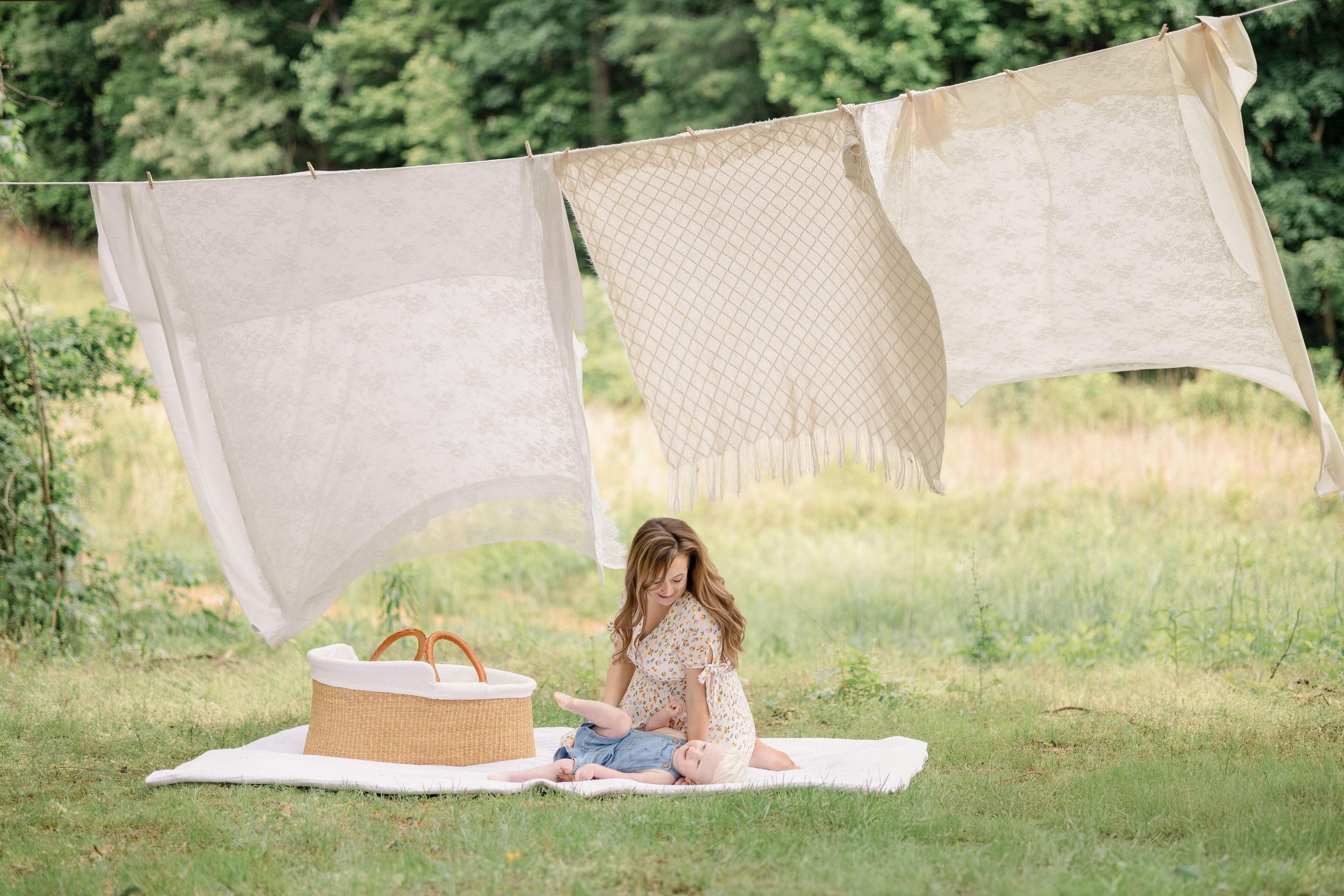 A person sits on a white blanket in a grassy outdoor setting while reading a book in natural sunlight.