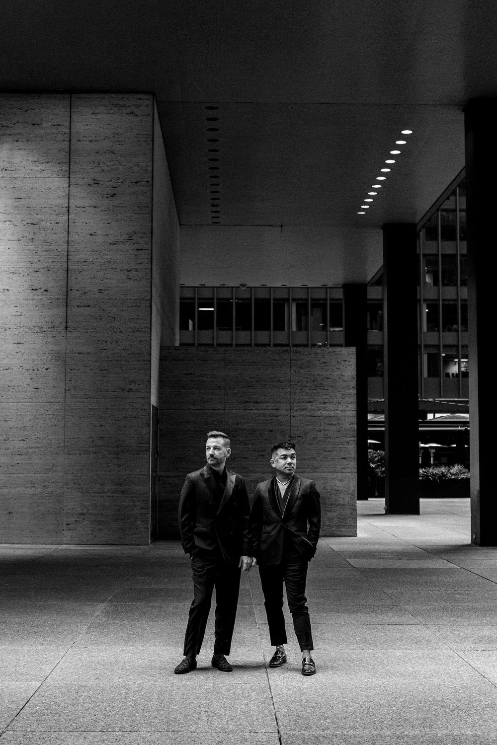 Black and white architectural photo of two people standing together in a modern building courtyard with concrete walls.