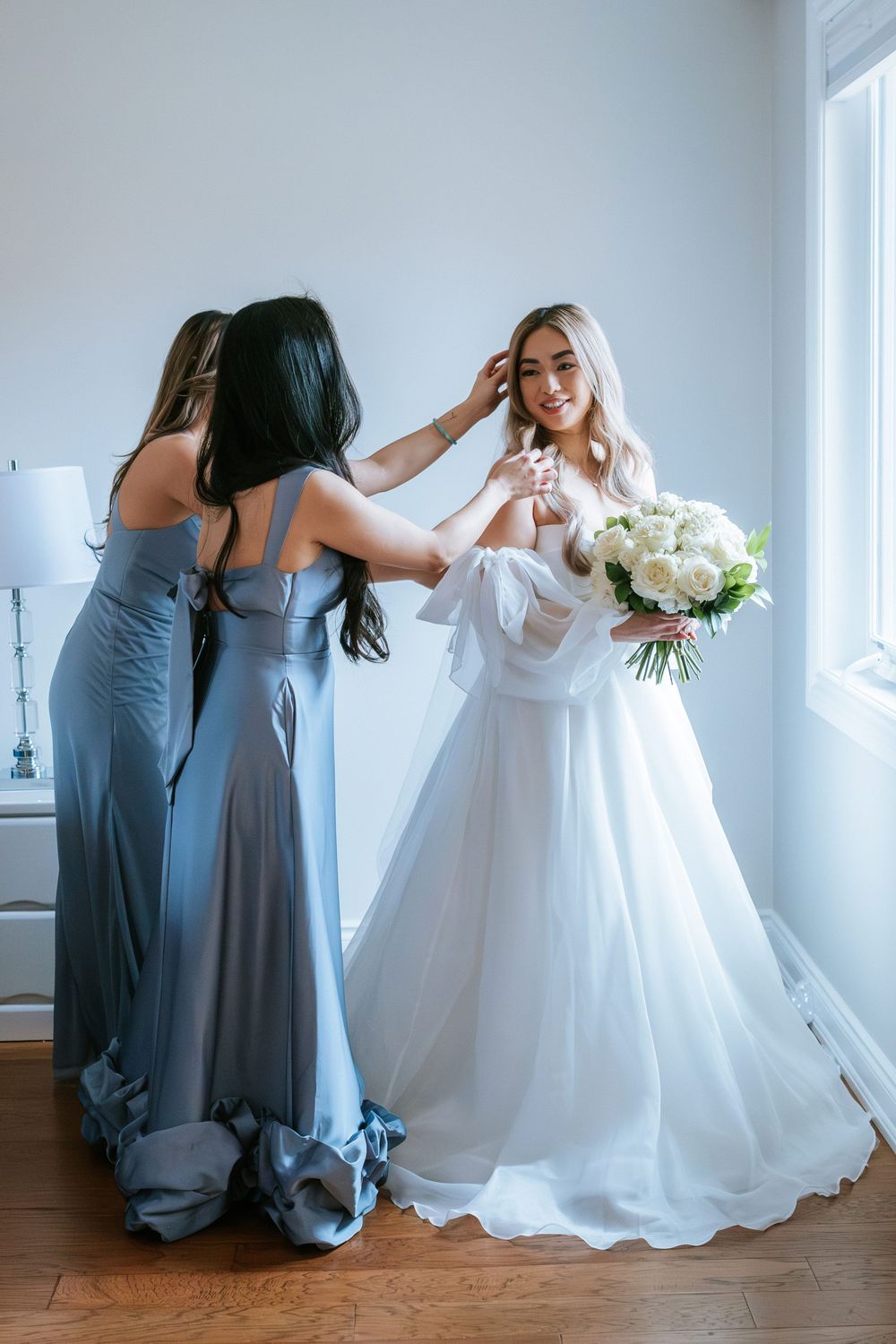 A series of candid wedding moments showing bridesmaids in blue dresses helping adjust the bride's white gown.